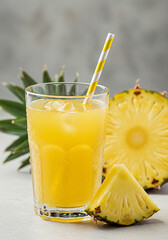 Glass of fresh pineapple juice with ice cubes and striped straw, surrounded by pineapple slices – tropical summer drink, healthy beverage, natural refreshment concept