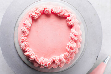Overhead view of Pink buttercream cake on a cake plate, top view of Cake covered in pink piping and...