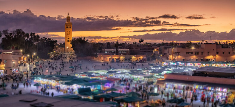 Tourists and locals crowding the vibrant Djemaa el Fna square in Marrakech, Morocco, with the Koutoubia Mosque minaret glowing at sunset