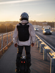 Man riding electric unicycle on sidewalk at sunset, back view