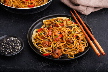 Asian food: Noodles with chicken and vegetables in teriyaki sauce on a dark background