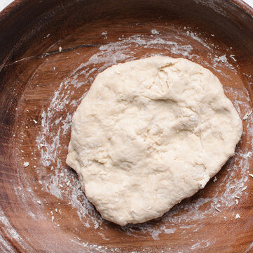 Overhead view of paratha dough being mixed in a wooden bowl, top view of flaky flatbread dough in a wood bowl, process of making paratha