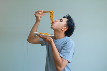 Happy young Asian man enjoying a plate of noodles with a cheerful expression, isolated on a clear background
