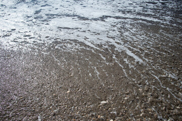 Foamy sea wave washing over a pebbly shore