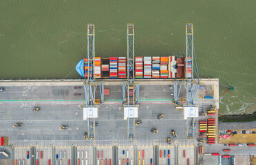 A container ship is unloaded by multiple trucks and added to the thousands of containers held at a...