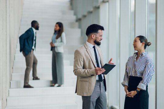 Business people discussing using digital tablet in office hallway