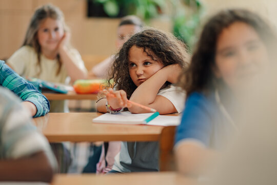 Bored elementary school student resting head on arms in classroom