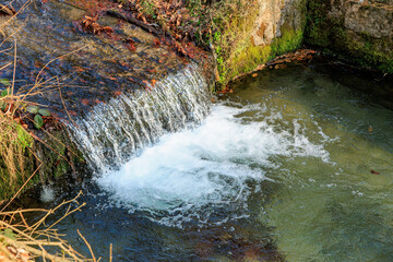 Serene small waterfall flowing into a clear stream through mossy rocks in nature