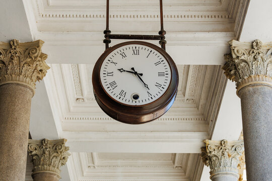 Vintage hanging clock with roman numerals between classical columns