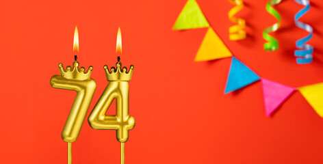 Number 74 birthday candle on an orange background with pennants