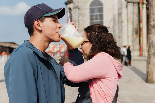 Two people lean over to drink from a glass.
