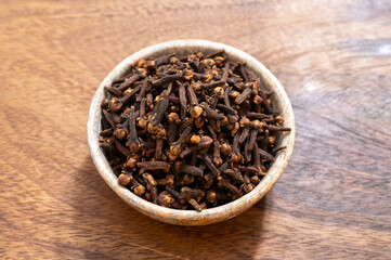 Stone bowl with dried clove buds, used for cooking and traditional medicine, close-up, spices collection