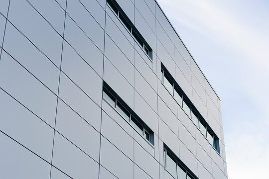 The exterior wall of a contemporary commercial style building with aluminum metal composite panels and glass windows. The futuristic building has engineered diagonal cladding steel frame panels.