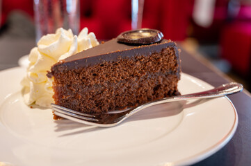 Piece of famous Sachertorte chocolate cake with apricot jam of Austrian origin served with whipped cream in old classic cafe-restaurant in Vienna