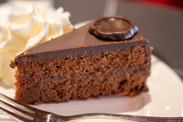 Piece of famous Sachertorte chocolate cake with apricot jam of Austrian origin served with whipped cream in old classic cafe-restaurant in Vienna
