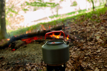 Tourist gas kettle on the background of live fire. Camping with a gas kettle. a kettle boiling on a...