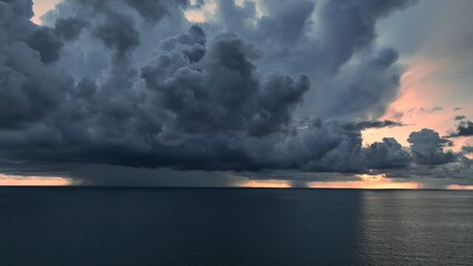 Aerial view captures the immense scale of a storm forming over the ocean, dark clouds swirling ominously as rain begins to fall, demonstrating nature's raw energy.
