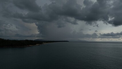 The aerial view reveals a massive rainstorm dominating the ocean, with sheets of rain falling from thick, menacing clouds, making the ocean appear turbulent and chaotic.
