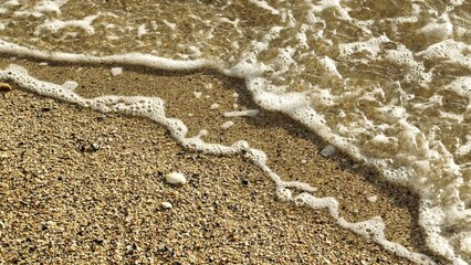Captured in slow motion, the water rushes to the shore, its foamy edges blending with the grains of sand, highlighting the ocean's delicate embrace of the beach.
