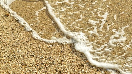 The slow-motion capture highlights the soft wave as it gently crashes against the golden sand, with foam swirling around seashells, evoking a sense of peace and tranquility.
