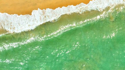 An aerial view of the beach, where the vibrant green waves meet the golden shore, showcasing the beautiful contrast between the ocean and the sand. Thailand.
