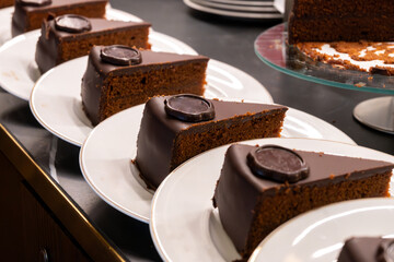 Many white plates with pieces of famous Sachertorte chocolate cake with apricot jam of Austrian origin in kitchen of old classic cafe-restaurant in Vienna