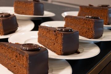 Many white plates with pieces of famous Sachertorte chocolate cake with apricot jam of Austrian origin in kitchen of old classic cafe-restaurant in Vienna
