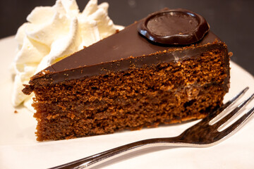 Piece of famous Sachertorte chocolate cake with apricot jam of Austrian origin served with whipped cream in old classic cafe-restaurant in Vienna