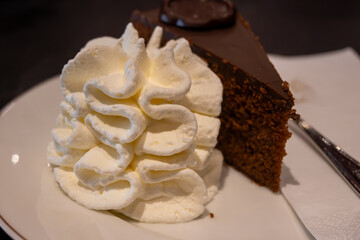 Piece of famous Sachertorte chocolate cake with apricot jam of Austrian origin served with whipped cream in old classic cafe-restaurant in Vienna