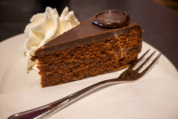 Piece of famous Sachertorte chocolate cake with apricot jam of Austrian origin served with whipped cream in old classic cafe-restaurant in Vienna