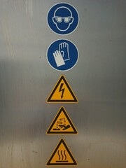 Safety warning signs on metal surface: mandatory use of goggles and gloves, and caution for...