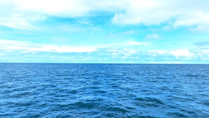 An endless view of the tropical sea from above, where the vast, shimmering blue waters stretch as...