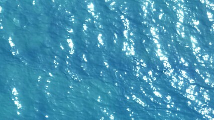 This aerial shot reveals the peaceful flow of water, where sunlight reflects and glistens across the surface. The ocean's vibrant blue turquoise color contrasts beautifully with the radiant glow.
