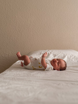 Playful little newborn lying on bed alone