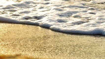 A close-up shot of ocean waves gently lapping against the shore, capturing the sparkling, golden reflection of the water. Ideal for beach, relaxation, or coastal travel content.
