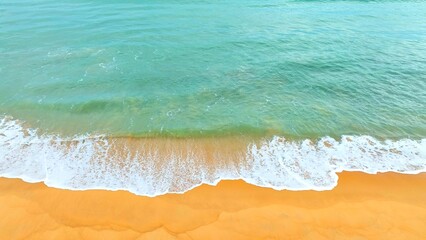 A stunning aerial shot of the clear green ocean waters blending with golden sand, with gentle waves lapping the shore, perfect for beach, nature, and tranquil coastal scenes. Phuket, Thailand.
