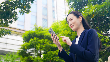新緑の街でスマホを使う女性ビジネスパーソン