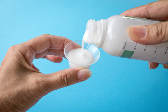 Pouring liquid medicine or antacid onto cup. Isolated on blue background.