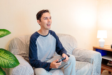 Young man smiling while playing video games at home in a cozy living room, enjoying a relaxed moment.