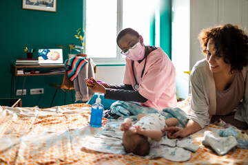 Nurse helping new mom at home with newborn baby
