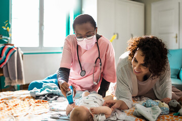 Nurse taking baby's temperature during home visit with mother
