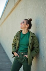 Obraz premium Joyful teenage girl in stylish green clothes laughs happily against concrete wall. Urban lifestyle. Fashionable woman, modern makeup, positive emotion. Trendy outfit, city background.