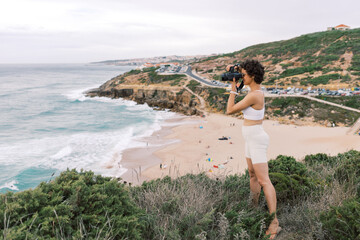 Woman taking a photo of São Julião Beach in Ericeira from a ciff