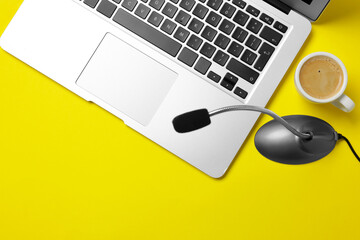 Professional microphone, laptop and coffee on yellow background, flat lay. Space for text