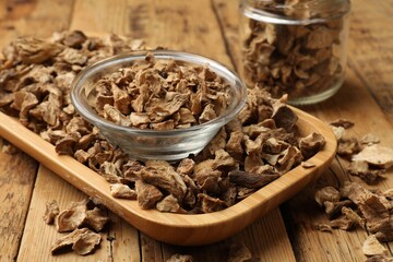 Pieces of dry chicory roots in bowl and jar on wooden table, closeup