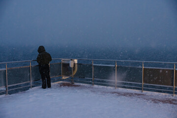 Person standing on snowy deck during snowfall at sea