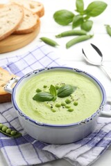 Tasty pea cream soup with basil served on white table