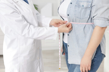 Weight loss. Nutritionist measuring overweight woman's waist with tape in clinic, closeup