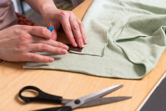 Hands measuring green fabric with ruler and chalk