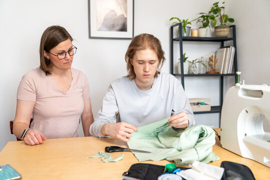 Teenager inspecting green fabric while woman watches